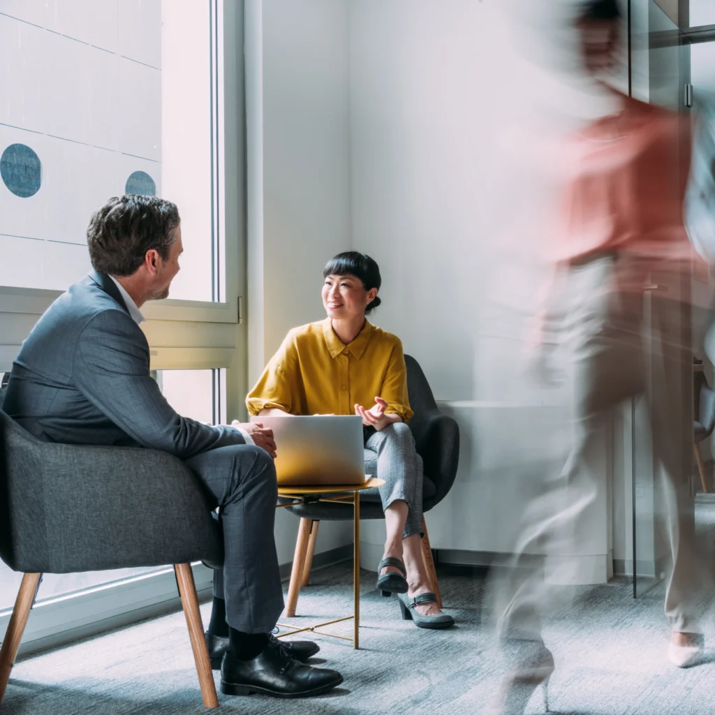 Shot of business people having a meeting in board room. Blurred motion of energetic businesspeople on the move and project team members discussing ideas in a modern office. Businesspeople walking in blurred motion around their colleagues. Business persons having a business meeting in office lobby while their colleagues are walking in blurred motion. Creative business team on meeting in the office.