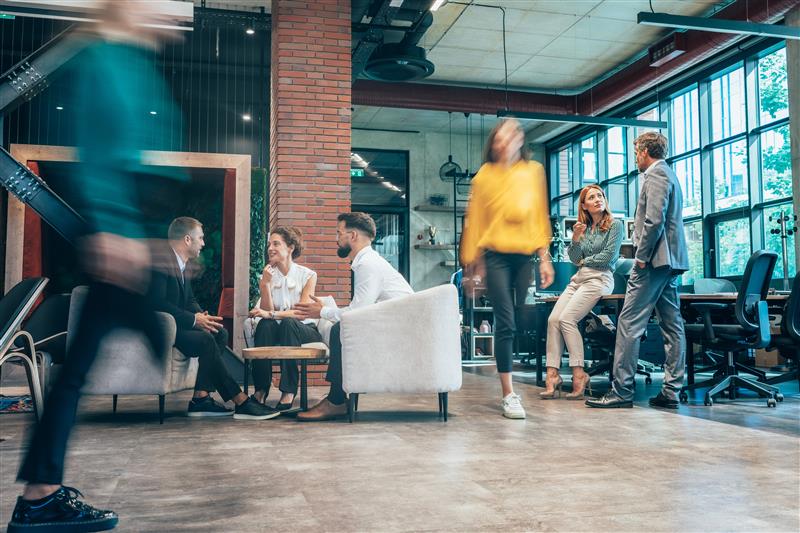 Businesspeople in modern open space office and Colleagues Walking By. Blurred motion of colleagues walking briskly down office hallway as colleagues sit and discussing ideas. Busy modern workplace. Working process in the office, business people working, walking and talking, blurred motion